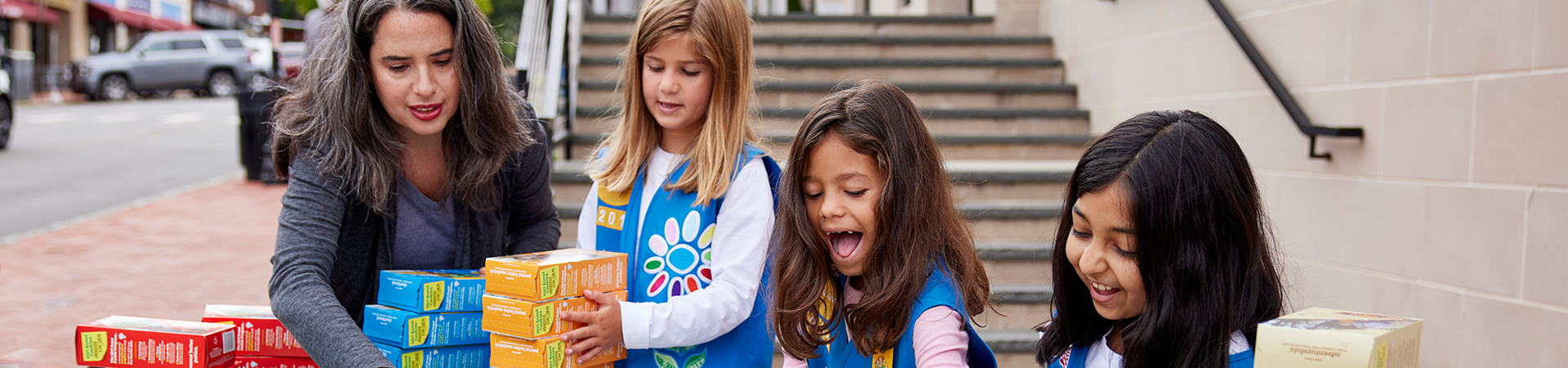  hands of young girl scout holding cookie boxes next to cookie transporter 